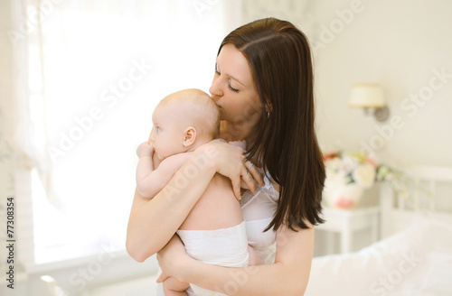 Happy mom gently hugs and kissing baby at home