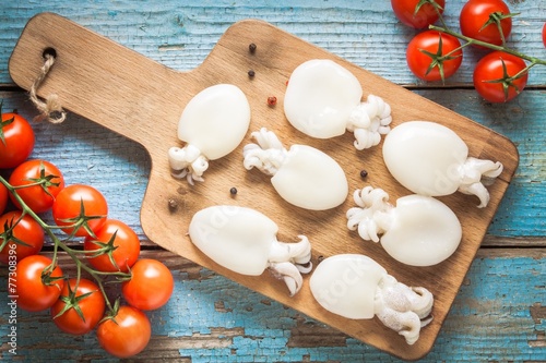 Φωτογραφία Raw babies cuttlefish  on a cutting board with tomatoes