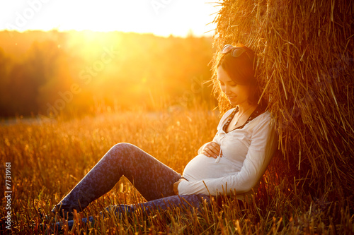 Young Pregnant Woman Sitting by the Haystack