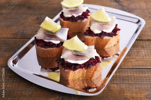 Rye toasts with herring and beets on tray on wooden background