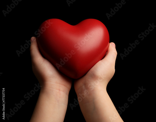 Heart in child hands on black background