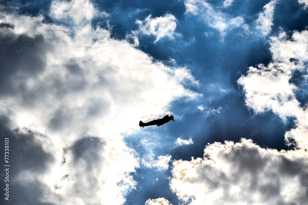 Spitfire silhouette on dark blue sky and snow white clouds Spitfire silhouette on dark blue sky and snow white clouds