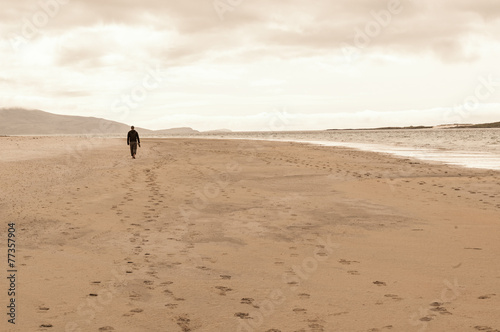 Solitary man taken from behind walking in an empty beach.