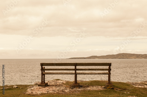 Old bench facing an open view with sea and faraway mountains.