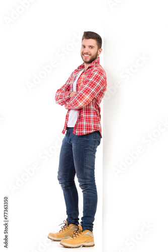 Smiling man in lumberjack shirt leaning on the white wall
