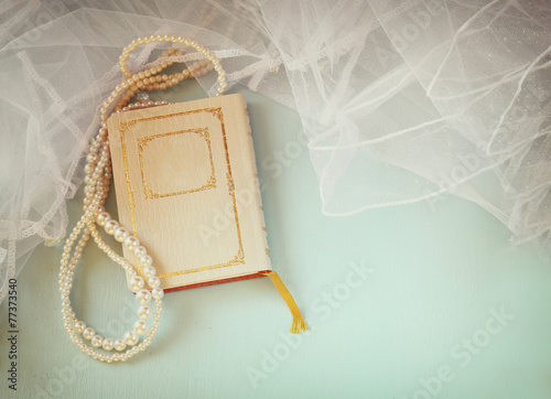 top view of old book and woman necklace over wooden table.