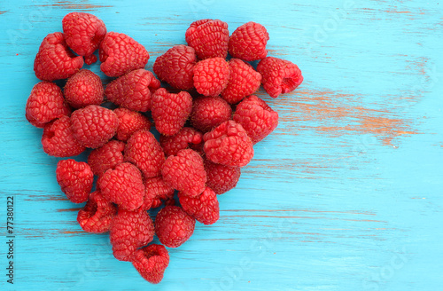 raspberries in a heart shape on blue wooden background photo