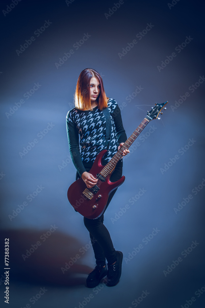 European appearance brown hair girl playing guitar on a gray bac European appearance brown hair girl playing guitar on a gray bac