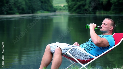 Young man lying in a deckchair near lake and drinking refershing bevarage photo