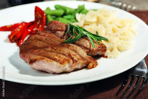 Steak with vegetables and pasta on plate on wooden plate