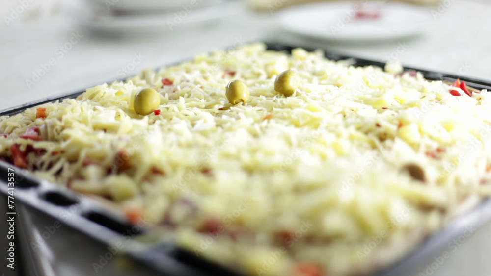 Close up shot of a black baking sheet with dough and a person who is putting on different kinds of ingredients for pizza Close up shot of a black baking sheet with dough and a person who is putting on different kinds of ingredients for pizza