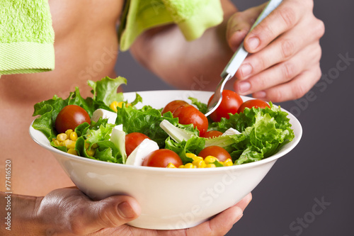 Fit man holding a bowl of fresh salad on grey background