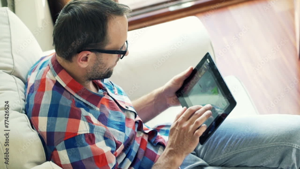 Man browsing photos on tablet computer sitting on sofa Man browsing photos on tablet computer sitting on sofa