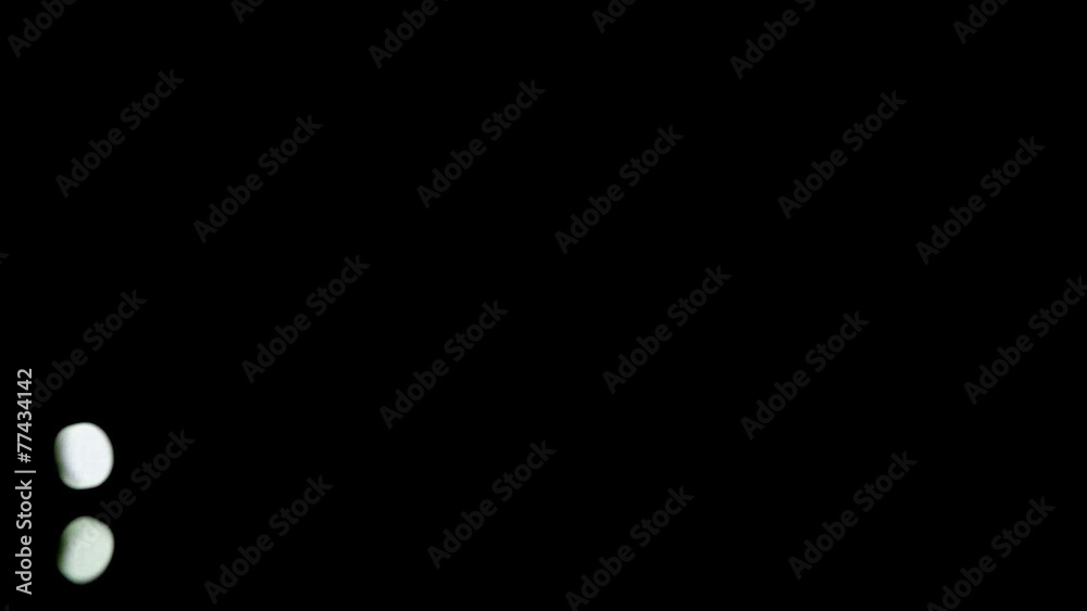 Two white tablets fall on and bounce of black surface Two white tablets fall on and bounce of black surface