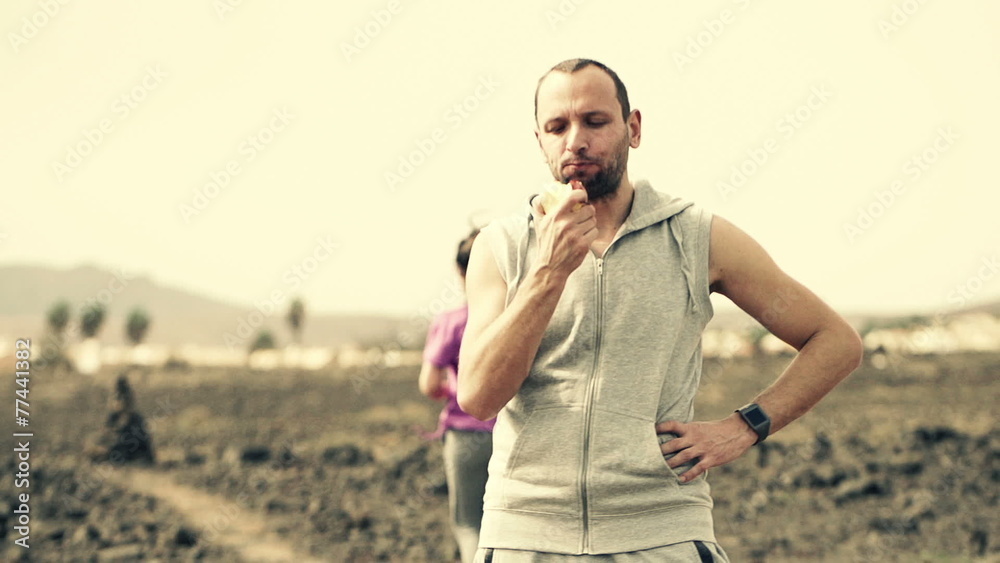 Man eating apple and woman jogging on desert Man eating apple and woman jogging on desert