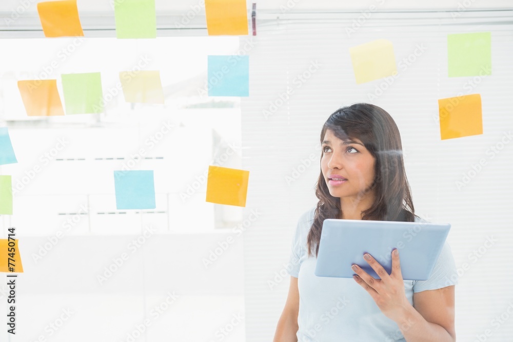 Businesswoman holding tablet and reading sticky notes Businesswoman holding tablet and reading sticky notes