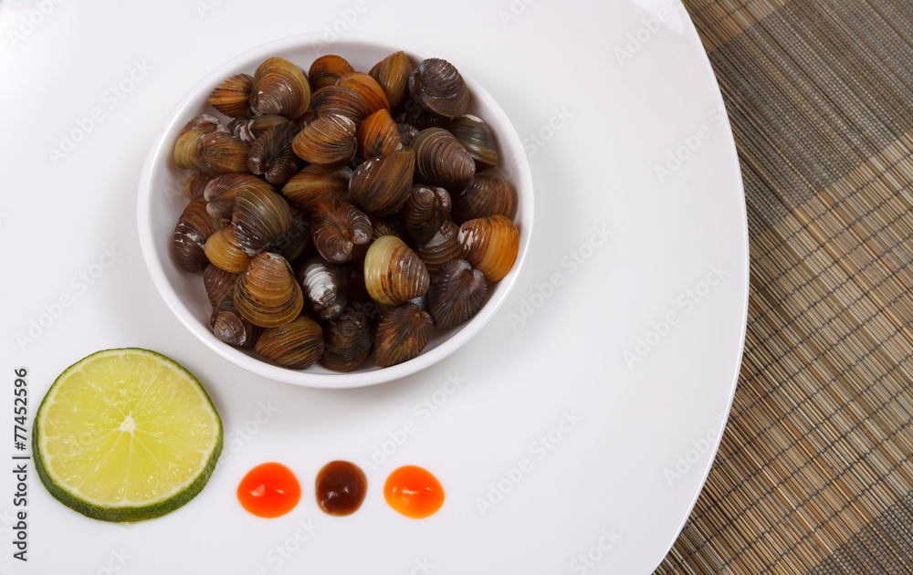 A plate with uncooked mussels and lime with sauces on a brown A plate with uncooked mussels and lime with sauces on a brown