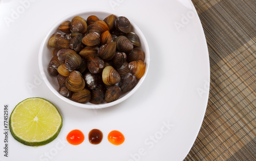 A plate with uncooked mussels and lime with sauces on a brown