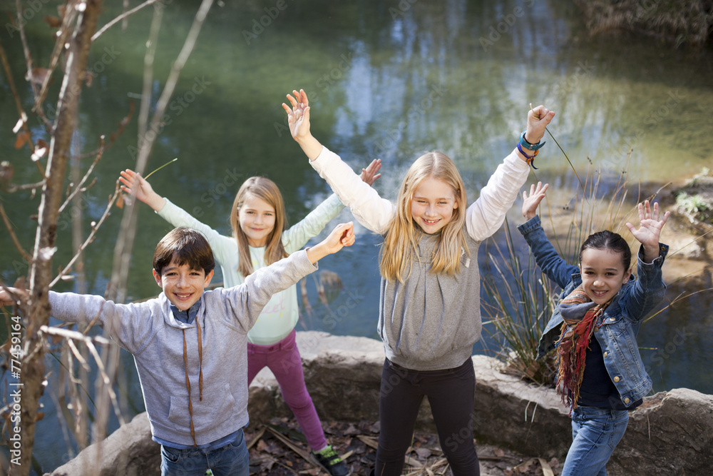 Niños junto a río levantando los brazos - obrazy, fototapety, plakaty 
