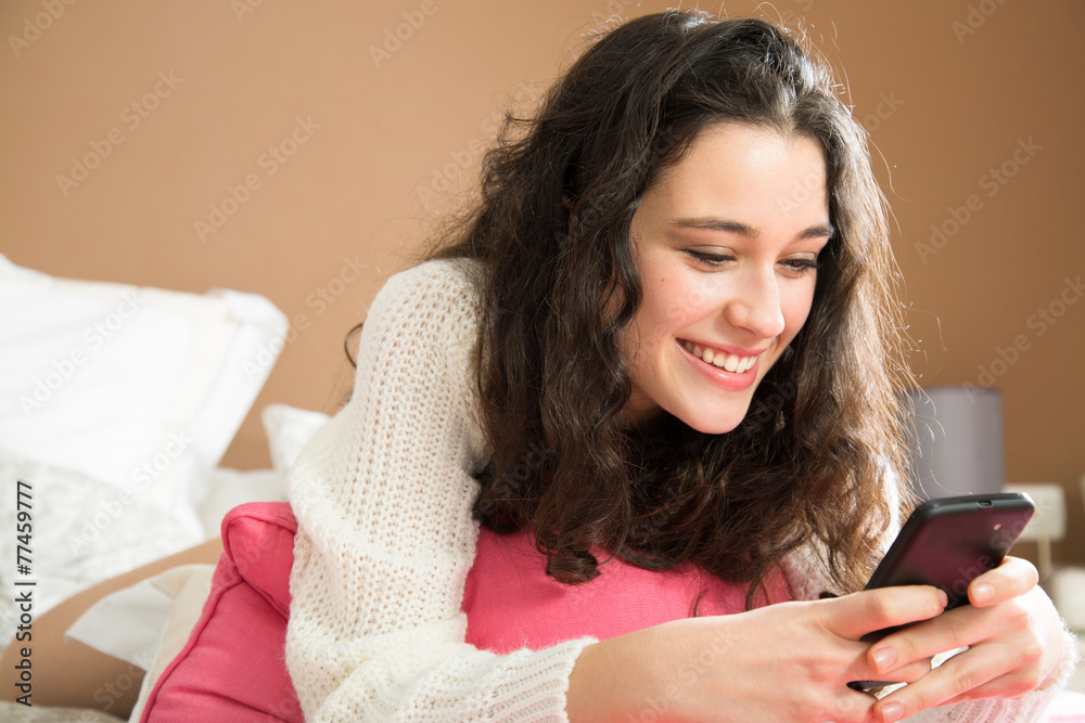 Happy young woman using mobile in bed
