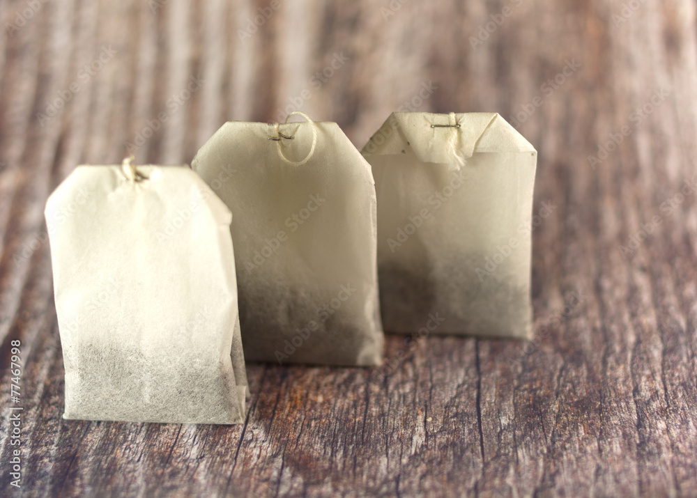 Three tea bags in raw on wooden background