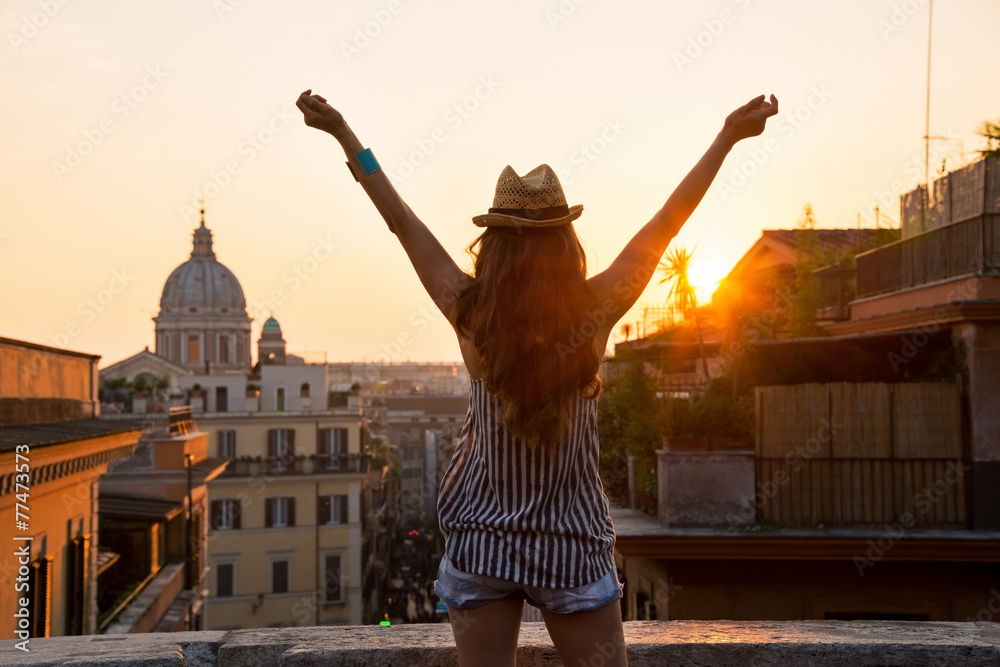 Naklejka premium Młoda kobieta, patrząc na dachy Rzymu na zachód słońca i radość.