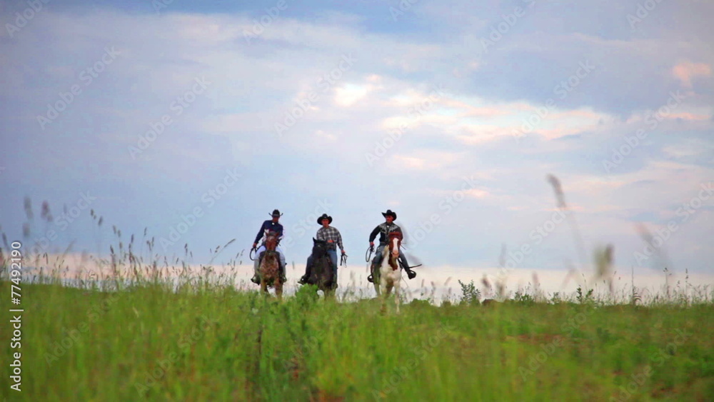 Three young cowboys jump on horses towards to viewer across fiel Three young cowboys jump on horses towards to viewer across fiel