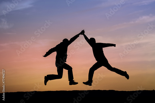 Two man holding for hands and jumping.