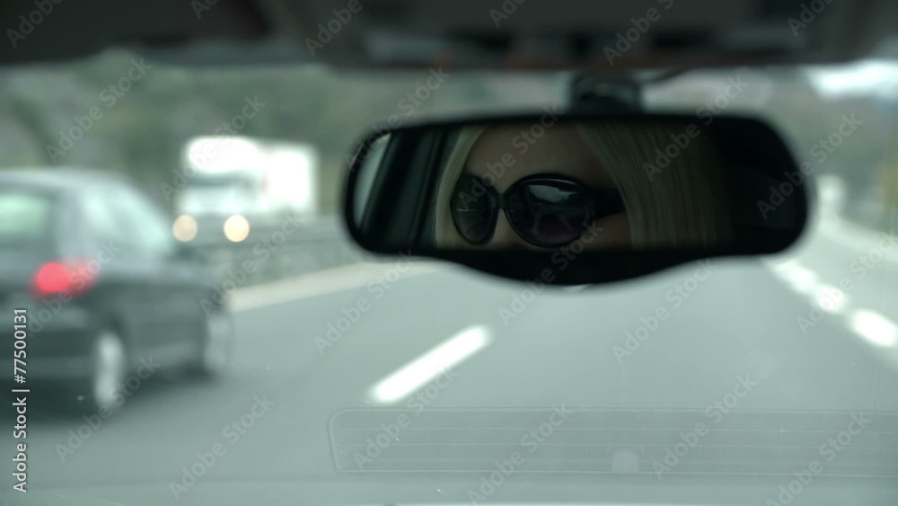 Shot of woman with sunglasses visible in rearview mirror driving towards tunnel Shot of woman with sunglasses visible in rearview mirror driving towards tunnel