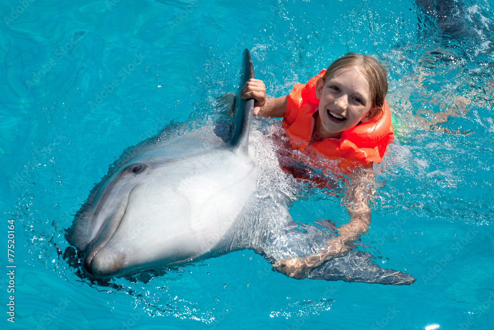 Obraz premium Happy Little Girl Riding the Dolphin in Swimming Pool