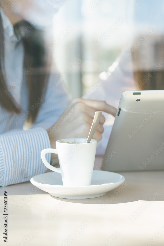 Closeup of coffee cup and girls using a tablet in coffee shop Closeup of coffee cup and girls using a tablet in coffee shop