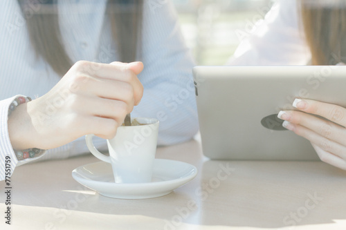 Closeup of coffee cup and girls using a tablet in coffee shop