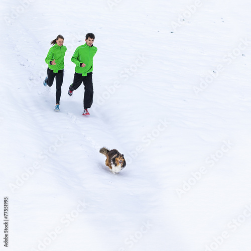 junger Mann und Frau joggen mit Hund in verschneiter Landschaft