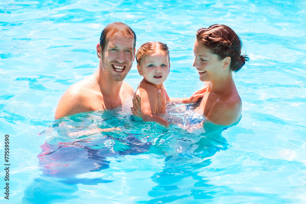 Happy family in swimming pool with baby girl