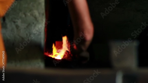 Close up slide shot of the furnace with sparkles and blacksmith takes out the metal and starts shaping the metal photo