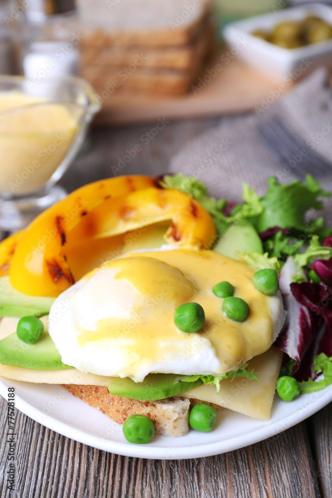 Toast with egg Benedict and avocado on plate on wooden table