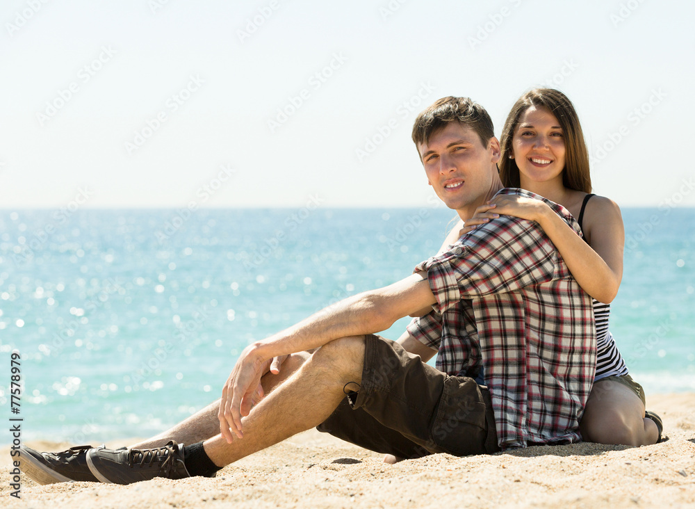  smiling couple sitting on the sea sand