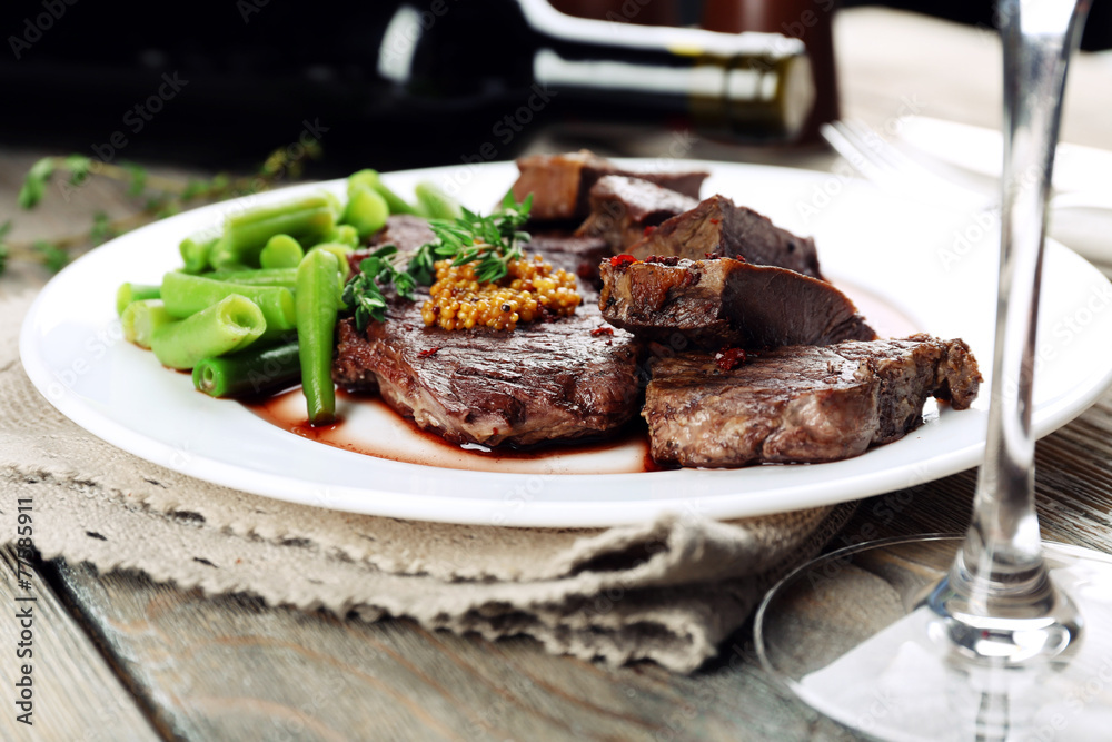 Steak on plate with bottle of wine on wooden background