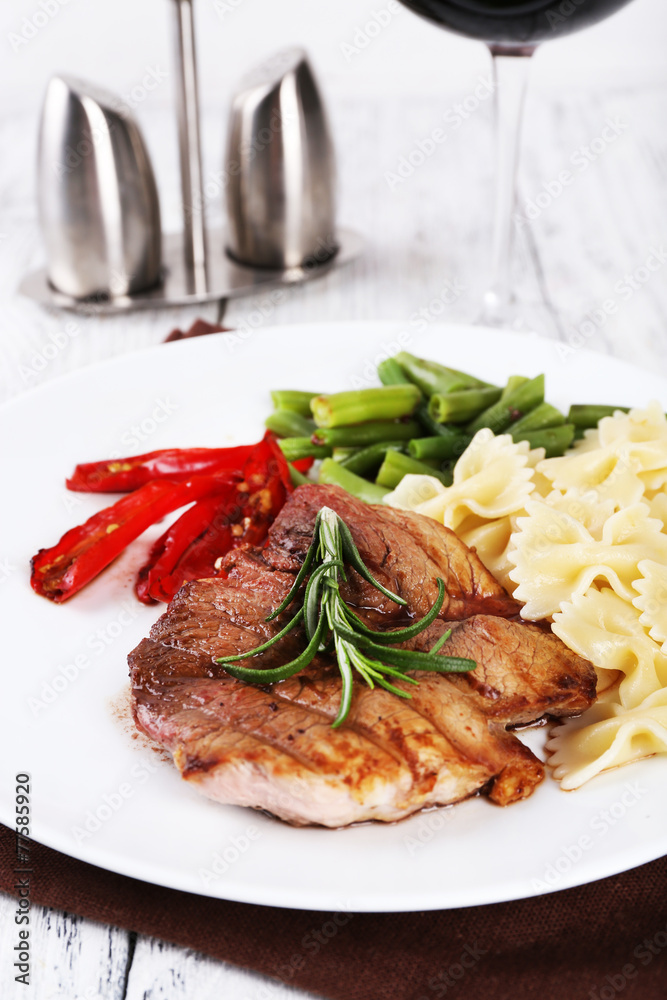 Steak with vegetables and pasta on plate on wooden plate