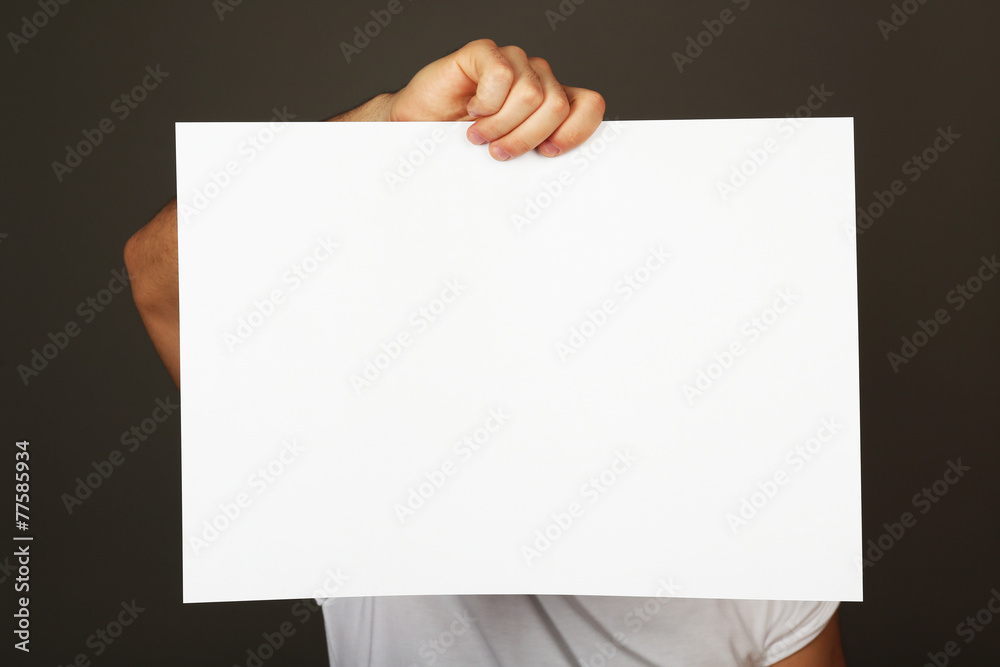 Blank sheet of paper in male hand on dark background Blank sheet of paper in male hand on dark background