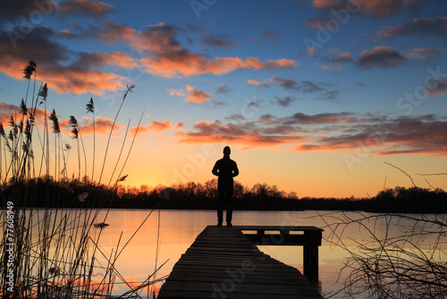 Fototapeta Naklejka Na Ścianę i Meble -  Man on a  jetty enjoying the winter sunset over a lake.