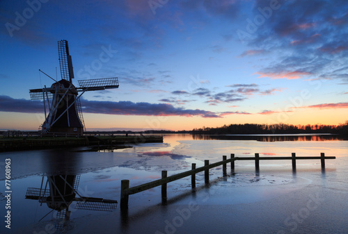 Traditional, Dutch windmill at a lake during winter sunset