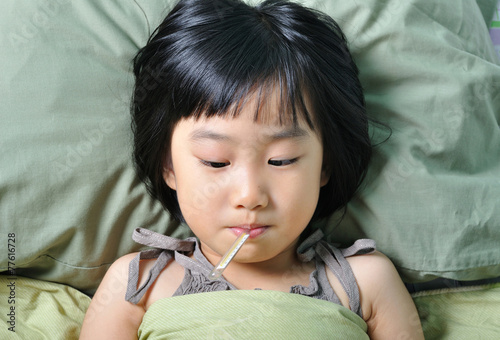 Little asain sick girl under blanket with temperature in mouth