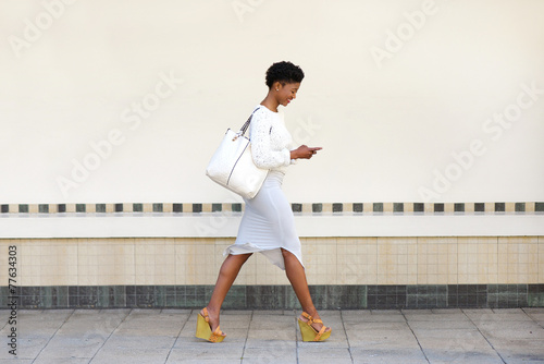 Young woman walking and sending text message on cell phone