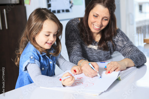 A mother and daughter drawing in a book on the kitchen