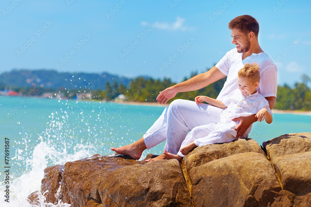 water splashing on laughing father and son on rocky coast
