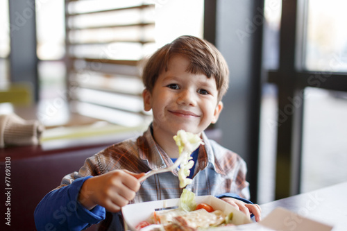 Little boy eating salad in fast food restaurant