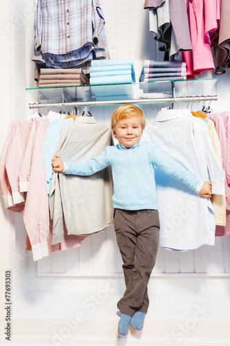 Boy standing among clothes on hangers and shelf