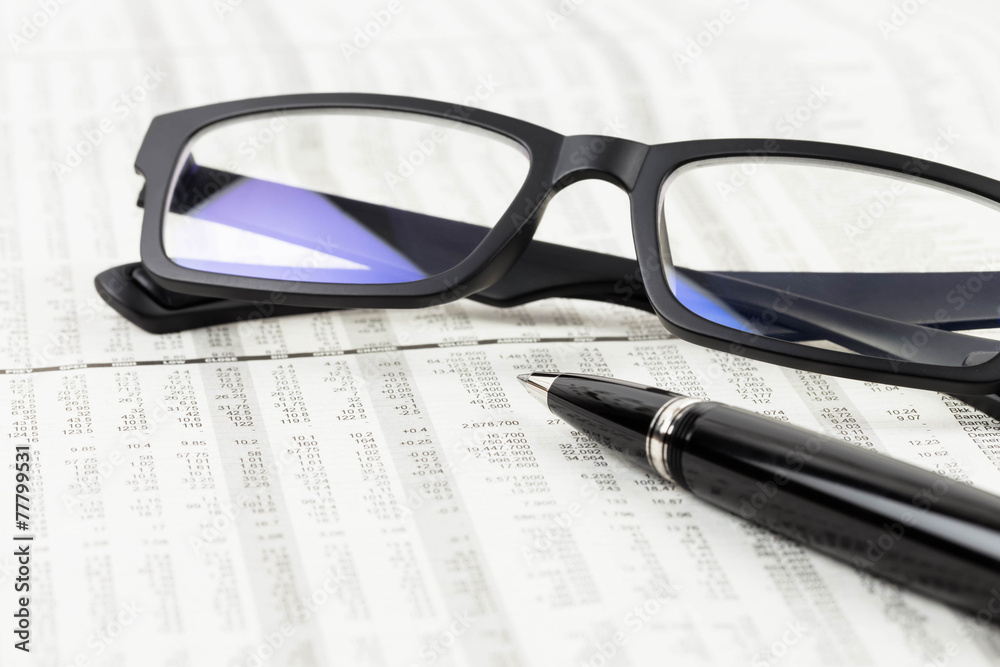 Pen and glasses rest on stock price detail financial newspaper Pen and glasses rest on stock price detail financial newspaper