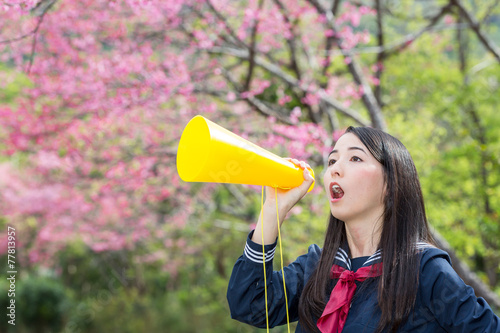 桜をバックにメガホンで応援をする女子学生